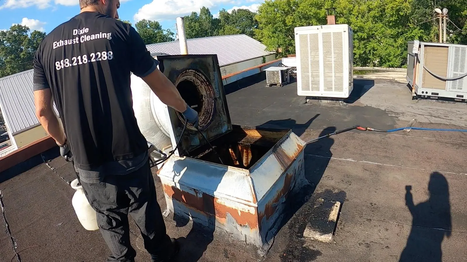A Dixie Exhaust crew member working inside an opened rooftop exhaust fan
